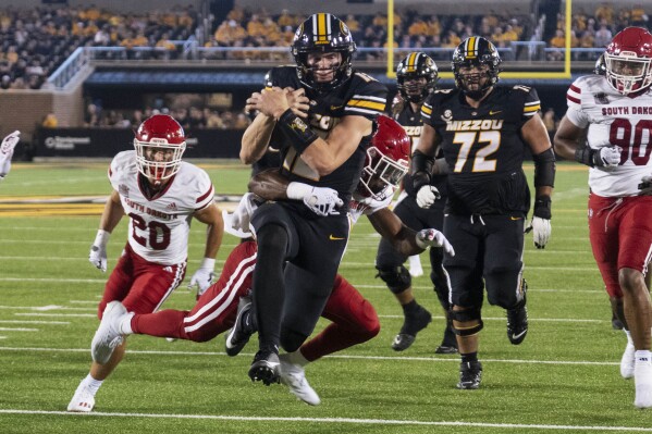 Missouri quarterback Brady Cook, center front, scores a touchdown as he is hit by South Dakota defensive back Teven McKelvey during the second quarter of an NCAA college football game Thursday, Aug. 31, 2023, in Columbia, Mo. (AP Photo/L.G. Patterson)