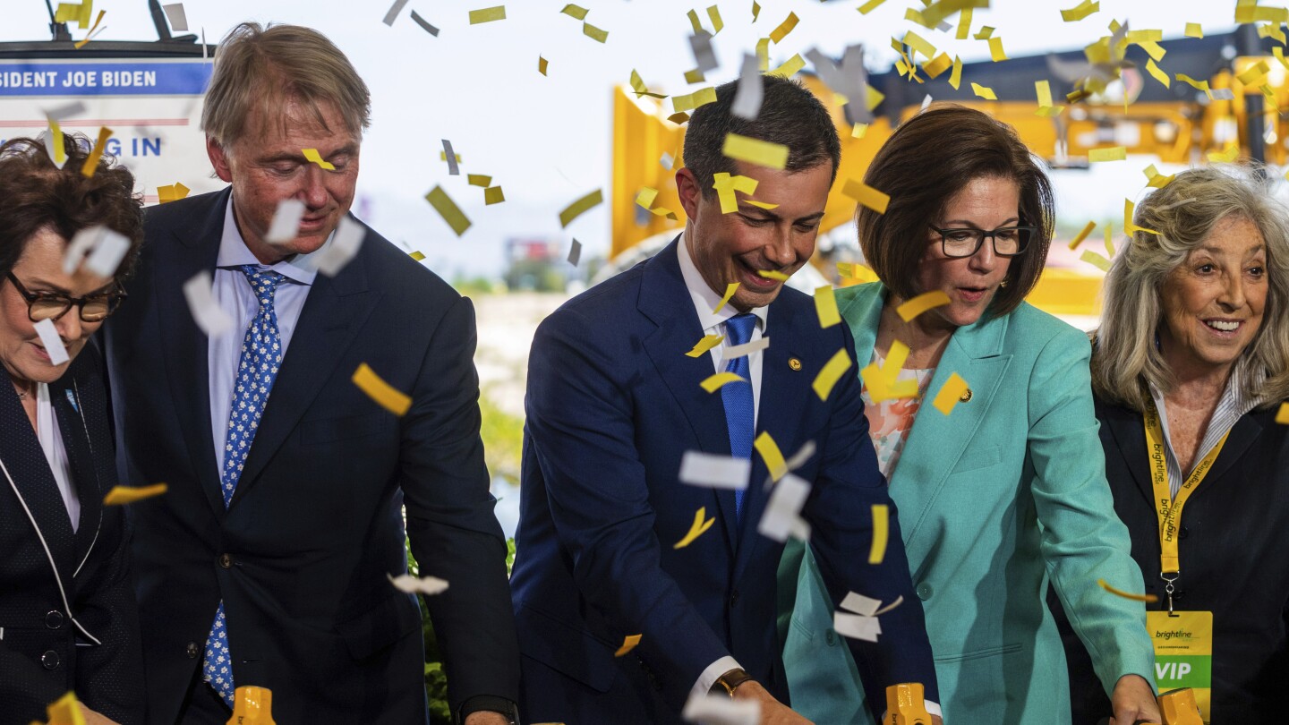 U.S. Secretary of Transportation Pete Buttigieg, center, Sen. Catherine Cortez Masto, right, drive rail spikes into a symbolic rail, on Monday, April 