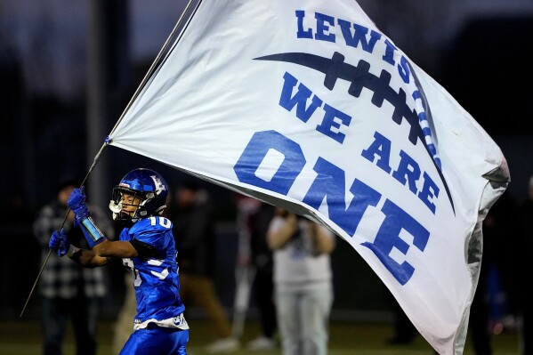 Lewiston High School running back Jayden Sands carries a flag onto the field prior to a football game against Edward Little High School, Wednesday, Nov. 1, 2023, in Lewiston, Maine. Locals seek a return to normalcy after a mass shooting on Oct. 25. (AP Photo/Matt York)
