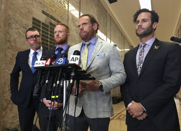 Curtis Briggs, second from right, the attorney for Max Harris, speaks at the courthouse in Oakland, Calif., Thursday, Sept. 5, 2019. A jury has acquitted Max Harris of involuntary manslaughter but couldn't reach a verdict for the leader of an artists' commune accused of turning a California warehouse into a cluttered maze that trapped 36 partygoers during a fast-moving fire. (AP Photo/D. Ross Cameron)