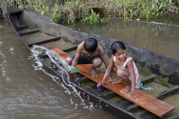 Indigenous Wari' children throw out water from a boat in the Komi Memem River, named Laje in non-Indigenous maps, in Guajara-Mirim, Rondonia state, Brazil, Friday, July 14, 2023. (AP Photo/Andre Penner)