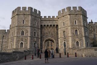 FILE - People take photos as police officers patrol the entrance of Windsor Castle, in Windsor, near London, Friday, Feb. 11, 2022. The British Army said Tuesday, May 3, 2022 it has launched an urgent investigation after an intruder posing as priest reportedly spent the night at the barracks of troops who guard Queen Elizabeth II at Windsor Castle. (AP Photo/Alberto Pezzali, File)