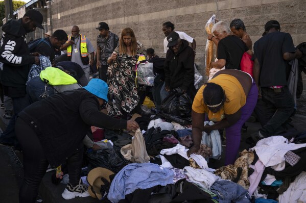 Homeless people gather around a pile of donated clothes to search for what they need in the Skid Row area of downtown Los Angeles, Thursday, Sept. 14, 2023. (AP Photo/Jae C. Hong)