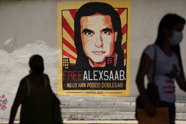 FILE - Pedestrians walk near a poster asking for the freedom of Colombian businessman and Venezuelan special envoy Alex Saab, in Caracas, Venezuela, Thursday, Sept. 9, 2021. The U.S. Justice Department is prosecuting Saab for alleged money laundering. (AP Photo/Ariana Cubillos, File)
