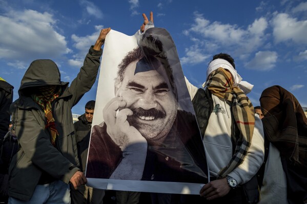 Youngsters hold a photograph of the jailed leader of the rebel Kurdistan Workers' Party, or PKK, Abdullah Ocalan as they gather to watch live on a tv screen a Pro-Kurdish Peoples' Equality and Democracy Party, or DEM, delegation members releasing an statement from Ocalan, in Diyarbakir, Turkey, Thursday, Feb. 27, 2025. (AP Photo/Metin Yoksu)