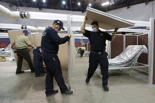 FILE — In this April 18, 2020 file photo partitions are installed between beds as work is performed to turn Sleep Train Arena into a 400-bed emergency field hospital to help deal with the coronavirus, in Sacramento, Calif. The state has reopened the arena and other facilities to help handle a new surge of coronavirus patients, but is using little more than a handful of volunteers from Gov. Gavin Newsom's California Health Corps who originally helped staff the facility. (AP Photo/Rich Pedroncelli, File)