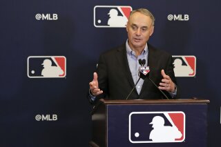 FILE - In this Feb. 8, 2019 file photo, Rob Manfred, commissioner of Major League Baseball, speaks during a news conference at owners meetings in Orlando, Fla. Major League Baseball and Reds are this season commemorating the 150th anniversary of the Cincinnati Red Stockings, who pioneered professional baseball. Manfred will be grand marshal Thursday, March 28 of the 100th Findlay Market Opening Day Parade in Cincinnati. The colorful parade featuring floats, marching bands and celebrities will begin winding through the city. (AP Photo/John Raoux, File)