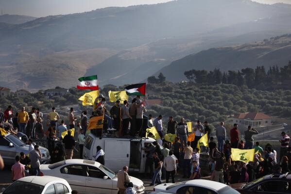 Hezbollah supporters wave their group, Iranian and Palestinian flags, during a protest in solidarity with Palestinians amid an escalating Israeli military campaign in Gaza, on the Lebanese-Israeli border in front of the Israeli settlement of Metula, background, near the southern village of Kafr Kila, Lebanon, Friday, May 14, 2021.   (AP Photo/Mohammed Zaatari)