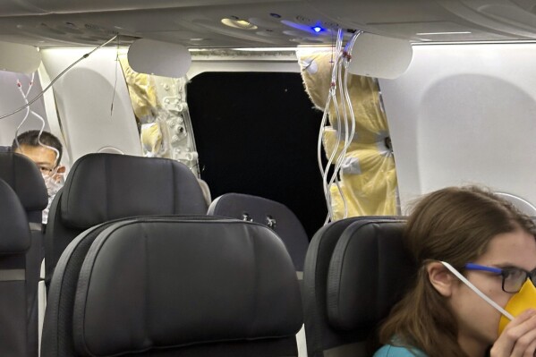 This image provided by Kelly Bartlett shows passengers near a hole in the fuselage of an Alaska Airlines Boeing 737 Max 9, Flight 1282, which was forced to return to Portland International Airport on Friday, Jan. 5, 2024. (Kelly Bartlett via AP)
