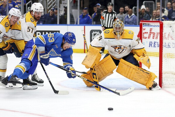 Nashville Predators goaltender Juuse Saros (74) defends as St. Louis Blues' Jake Neighbours (63) reaches for the puck during the second period of an NHL hockey game Saturday, Feb. 17, 2024, in St. Louis. (AP Photo/Scott Kane)