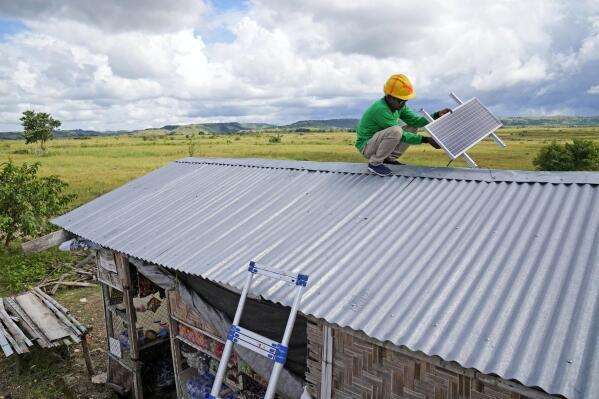 Antonius Makambombu, a worker of Sumba Sustainable Solutions performs maintenance work on a solar panel on the roof of a customer's shop in Laindeha village on Sumba Island, Indonesia, Wednesday, March 22, 2023. Working with international donors to help subsidize the cost, the company provides imported home solar systems, which can power light bulbs and charge cellphones, for monthly payments equivalent to $3.50 over three years. (AP Photo/Dita Alangkara)