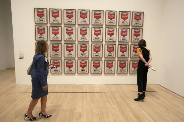 FILE- A pair of women look at the 1962 pop piece called "Campbell's Soup Cans" at the exhibition, "Andy Warhol _ From A to B and Back Again, in San Francisco on May 15, 2019. Climate protesters in Australia on Wednesday, Nov. 9, 2022 scrawled graffiti and glued themselves to an Andy Warhol artwork depicting Campbell's soup cans but didn't appear to damage the piece because it's encased in glass. (AP Photo/Eric Risberg, File)