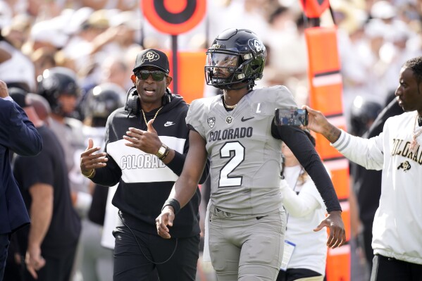 Colorado head coach Deion Sanders, left, talks with his son, quarterback Shedeur Sanders, before the first half of an NCAA college football game against Southern California, Saturday, Sept. 30, 2023, in Boulder, Colo. (AP Photo/David Zalubowski)