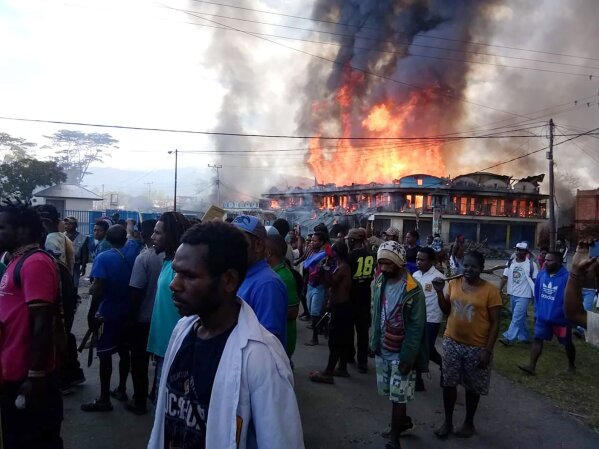 People gather as shops burn in the background during a protest in Wamena in Papua province, Indonesia, Monday, Sept 23, 2019. Hundreds of protesters in Indonesia's restive Papua province set fire to homes and other buildings Monday in a protest sparked by rumors that a teacher had insulted students, and a soldier was killed in another protest in the region, police said. (AP Photo)