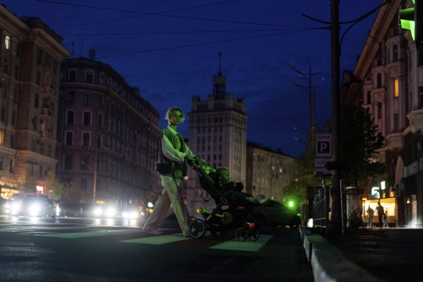 A woman pushes a cart carrying her child across a dark street after the municipality cut the city lights to conserve energy in Kharkiv, Ukraine, on Sunday, April 14, 2024. (AP Photo/Evgeniy Maloletka)