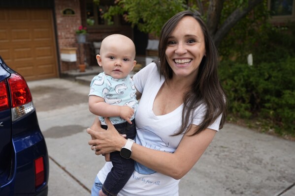 Carrie Martin-Haley holds her son outside their home Friday, May 10, 2024, in Greenwood Village, Colo. Colorado's paid family and medical leave benefits kicked in on Jan. 1, too late for Martin-Haley, a small business owner in Denver who gave birth to her son in September 2023. (AP Photo/David Zalubowski)