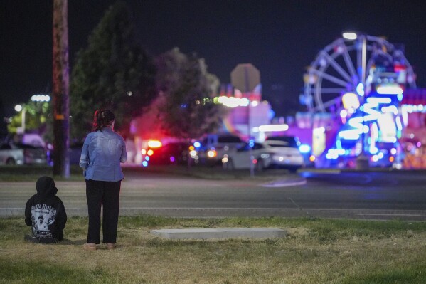 Onlookers watch as law enforcement investigate after a reported shooting at WestFest in West Valley City, Utah, June 15, 2025. (Chris Samuels/The Salt Lake Tribune via AP) **NOT AN AP MEMBER**