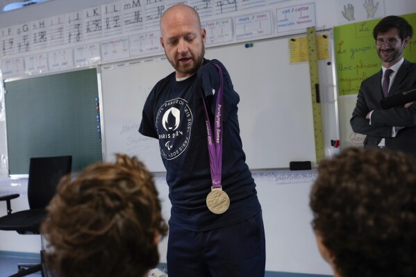 Archer Matt Stutzman of United States shows his silver medal from the Paralympic Games in 2012 to pupils, in a Paris school, in Paris, Wednesday, Oct. 4, 2023. Visiting France's capital before Paralympic tickets go on sale next week, Stutzman dropped by a Paris school on Wednesday and wowed its young pupils with his shooting skills. (AP Photo/Thibault Camus)