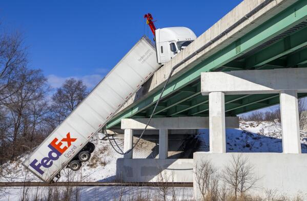 A FedEx semi comes to rest over train tracks after its trailer toppled over an Indiana Toll Road bridge on Interstate 80/90, at Currant Road, on Wednesday, Jan. 26, 2022, in Mishawaka, Ind. Near zero temperatures and icy roads caused multiple accidents in the area on Wednesday morning. (Robert Franklin/South Bend Tribune via AP)