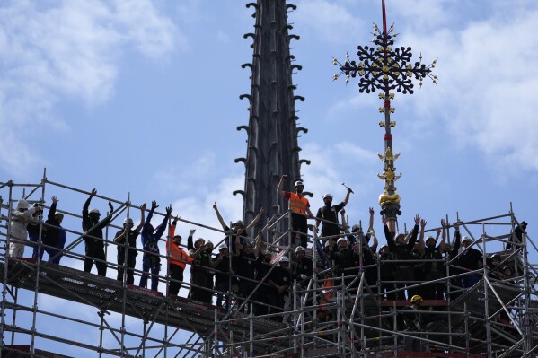 Workers celebrate after reinstalling the Notre Dame de Paris cathedral's Croix du Chevet, right, Friday, May 24, 2024, in Paris. The Croix du Chevet is the only piece of the cathedral roof that did not burn in the devastating April 2019 fire. (AP Photo/Thibault Camus)