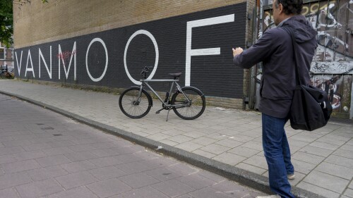 A man parked his VanMoof bicycle outside the VanMoof head office to take a picture in Amsterdam, Netherlands, Tuesday, July 18, 2023. Dutch electric bicycle maker VanMoof has been declared bankrupt, slamming the brakes on a company that won design awards for its pared-back electric bikes but struggled to meet soaring demand and fix glitches. (AP Photo/Peter Dejong)