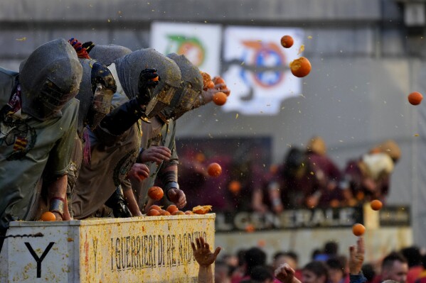 People wearing protection helmets and costumes pelt each other with oranges during the "Battle of the Oranges" part of Carnival celebrations in the northern Italian Piedmont town of Ivrea, Italy, Tuesday, Feb. 13, 2024. (AP Photo/Antonio Calanni)
