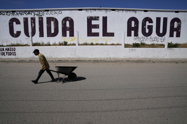 A man passes an empty water storage building emblazoned with the slogan, "conserve water," in Spanish, Tuesday, May 9, 2023, in Tijuana, Mexico. Among the last cities downstream to receive water from the shrinking Colorado River, Tijuana is staring down a water crisis. (AP Photo/Gregory Bull)