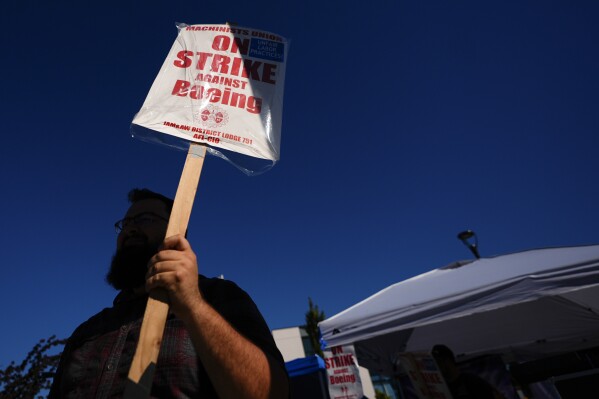 A Boeing worker waves a picket sign Tuesday, Sept. 24, 2024, as workers continue to strike outside the company's factory in Renton, Wash. (AP Photo/Lindsey Wasson)