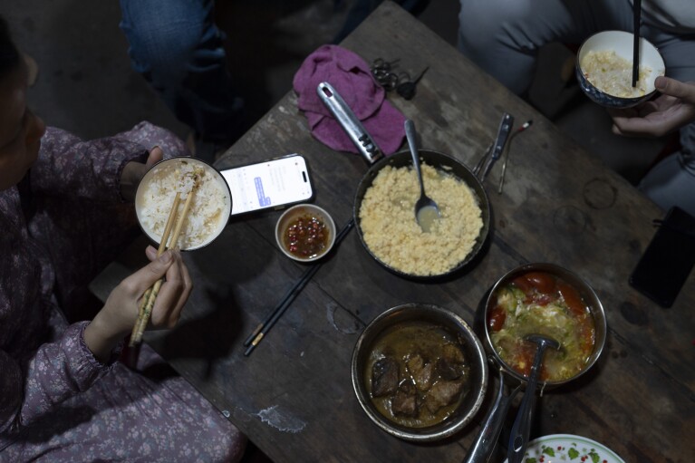 2024 年 1 月 24 日星期三，一家人在越南胡志明市的商店外吃晚餐。大米不仅是大多数膳食的主食，它还被认为是神的礼物，并且一直受到人们的崇拜。  （美联社照片/Jae C. Hong）