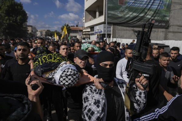 Mourners carry the bodies of three Palestinians draped in the Hamas and Islamic Jihad militant group flags during their funeral in the Jenin refugee camp, West Bank Friday, Nov. 17, 2023. Israeli forces killed the three men in an overnight raid, the Palestinian Health Ministry said Friday. The military wing of the Palestinian Islamic Jihad group claimed the three, including local commander Jamal Lahlouh, 23, as members. (AP Photo/Majdi Mohammed)