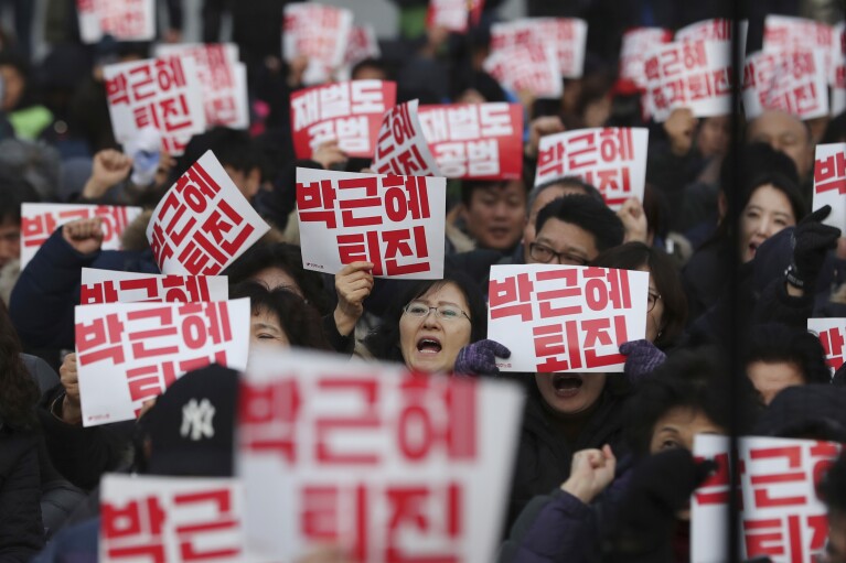 Protesters shout slogans during a rally calling for South Korean President Park Geun-hye to step down near the National Assembly in Seoul, South Korea, Wednesday, Dec. 7, 2016. A South Korean parliamentary committee sent a squad of security officers on Wednesday to order the jailed woman at the center of a scandal that threatens to bring down the president to attend a hearing investigating her alleged manipulation of government affairs. The letters read 