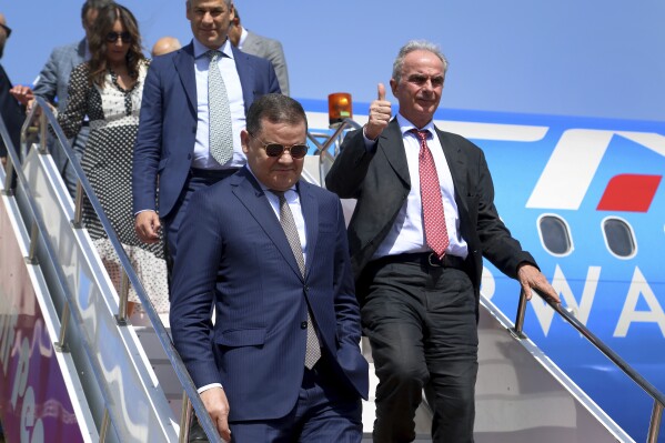 The prime minister of one of Libya's rival administrations, Abdul-Hamid Dbeibah, front, and the President of the Italian Civil Aviation Authority Pierluigi Di Palma, right, leave the airplane after their arrival in Tripoli, Libya, Monday, July 24, 2023, on the first direct flight between Italy and Libya in nearly a decade by a commercial airline. Oil-rich Libya plunged into chaos after a NATO-backed uprising toppled and killed longtime dictator Moammar Gadhafi in 2011. In the disarray that followed, the country split into rival administrations in the east and west, each backed by rogue militias and foreign governments, and much of the country's international air connections were cancelled. (AP Photo/Yousef Murad)