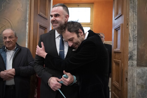 Greek author Petros Hadjopoulos, who uses the pen name Auguste Corteau, hugs his husband, lawyer Anastasios Samouilidis, before their wedding at Athens City Hall, Greece, on Thursday, March 7, 2024. A Greek novelist and his partner on Thursday became the first male couple to be married in Athens' city hall following the legalization of same-sex marriage in Orthodox Christian Greece. (AP Photo/Michael Varaklas)