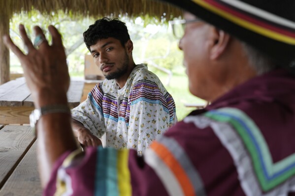 Hector Tigertail, a young member of the Miccosukee Tribe, listens to Tribal elder Michael Frank speak about the environmental degradation he has witnessed over his lifetime, and the importance of the Everglades homeland to Miccosukee history and identity, on the Miccosukee Indian Reservation in the Florida Everglades, Thursday, May 16, 2024. (AP Photo/Rebecca Blackwell)