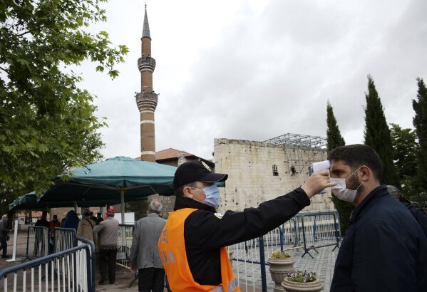 A security official checks a man's temperature as people, wearing face masks and observing social distancing guidelines to protect against coronavirus, wait to attend Friday prayers, outside historical Haci Bayram Mosque, in Ankara, Turkey, Friday, May 29, 2020. Worshippers in Turkey have held their first communal Friday prayers in 74 days after the government re-opened some mosques as part of its plans to relax measures in place to fight the coronavirus outbreak. (AP Photo/Burhan Ozbilici)