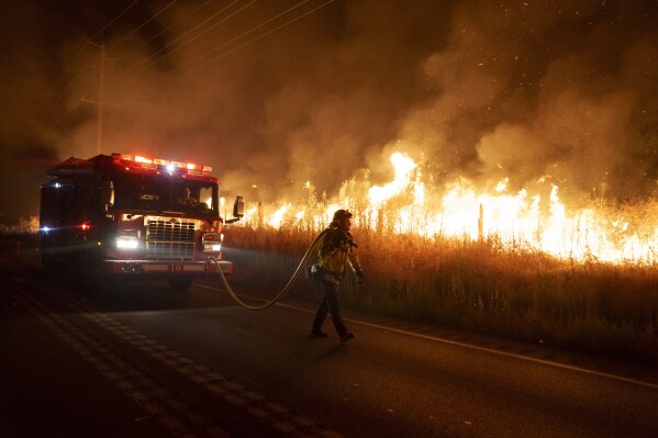 A firefighter watches flames approach Gilman Springs Road during the Rabbit Fire late Friday, July 14, 2023, in Moreno Valley, Calif. (AP Photo/Eric Thayer)