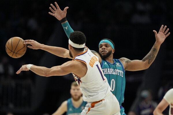 Phoenix Suns guard Devin Booker passes around Charlotte Hornets forward Miles Bridges during the first half of an NBA basketball game on Friday, March 15, 2024, in Charlotte, N.C. (AP Photo/Chris Carlson)