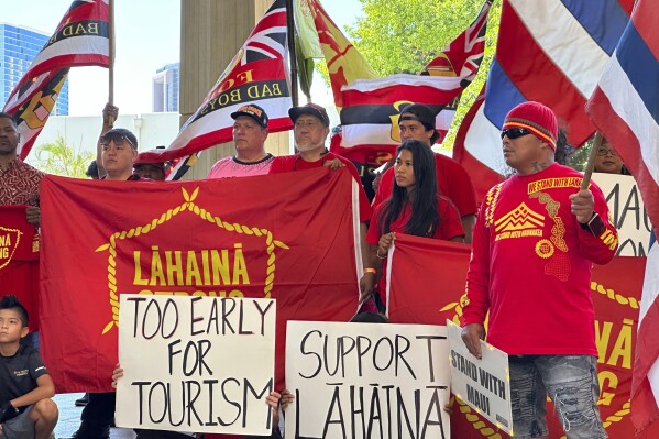 Lahaina residents and their supporters hold signs and flags at the Hawaii State Capitol in Honolulu on Tuesday, Oct. 3, 2023, at a news conference about a petition asking Hawaii Gov. Josh Green to delay plans to reopen a portion of West Maui to tourism starting this weekend. The petition signed by more than 14,000 people comes amid a fierce and anguished debate over when travelers should return to the region, home to the historic town of Lahaina that was destroyed in the deadliest U.S. wildfire in more than a century. (AP Photo/Audrey McAvoy)