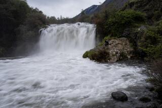 Ruben Onate takes pictures sitting next to the largest waterfall of the Truful Truful River, near Melipeuco, southern Chile, on Thursday, June 30, 2022. Mapuche people believe in the falling water's distinctive "energy power" for healing purposes, either in riverside ceremonies or by taking large soda bottles full of it back home. (AP Photo/Rodrigo Abd)