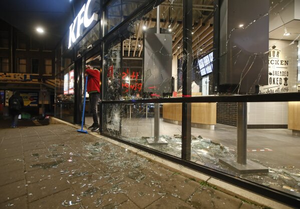 A man rests on his broom as he stands next to shards of glass and smashed windows of a fast-food restaurant that was damaged in protests against a nation-wide curfew in Rotterdam, Netherlands, Monday, Jan. 25, 2021. The Netherlands Saturday entered its toughest phase of anti-coronavirus restrictions to date, imposing a nationwide night-time curfew from 9 p.m. until 4:30 a.m. in a bid to control the COVID-19 infection rate. (AP Photo/Peter Dejong)