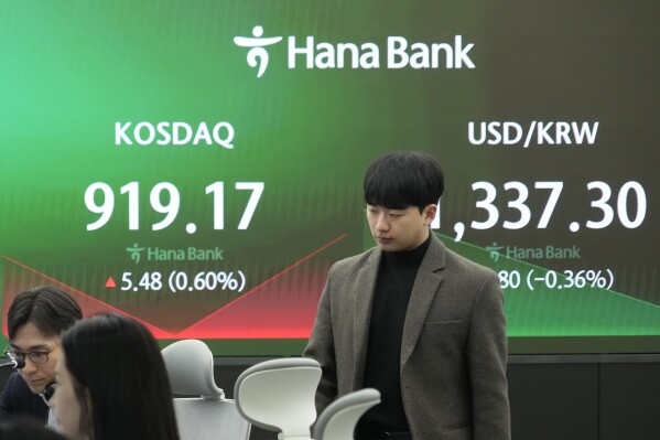 A currency trader passes by the screens showing the Korea Composite Stock Price Index (KOSPI), left, and the foreign exchange rate between U.S. dollar and South Korean won at the foreign exchange dealing room of the KEB Hana Bank headquarters in Seoul, South Korea, Tuesday, March 26, 2024. Asian shares were mixed in muted trading Tuesday, as buying in some markets was soon erased by profit-taking. (AP Photo/Ahn Young-joon)