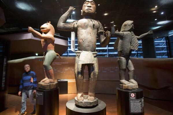 In this Friday, Nov. 23, 2018 file photo a visitor looks at wooden royal statues of the Dahomey kingdom, dated 19th century, at Quai Branly museum in Paris, France. France will return 26 African artworks to Benin later this month as part of long-promised efforts to give back artwork taken from Africa during the colonial era. (AP Photo/Michel Euler, File)