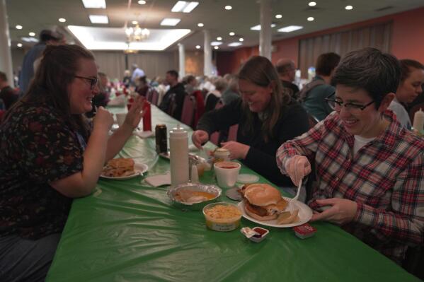 From left, Laura Kuster, Miranda Crotsley, and Hollen Barmer eat fish sandwiches, homemade perogies, and macaroni and cheese at the St. Maximilian Kolbe Catholic Church fish fry in the West Homestead neighborhood of Pittsburgh, on Friday, Feb. 24, 2023. To innovate the age-old tradition of fish fries, Barmer and volunteers from Code for Pittsburgh created the "Pittsburgh Lenten Fish Fry Map," an online interactive map that locates and documents active fish fries from year to year across Western Pennsylvania. (AP Photo/Jessie Wardarski)