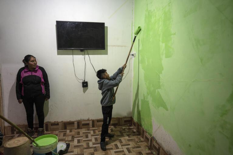 Elizabeth Mamani, 30, watches her son, Alexis, 10 paint the walls of their new house in Huancar, Jujuy Province, Argentina, April 25, 2023. The Andean town is prospering because of the work available in nearby lithium mines. (AP Photo/Rodrigo Abd)