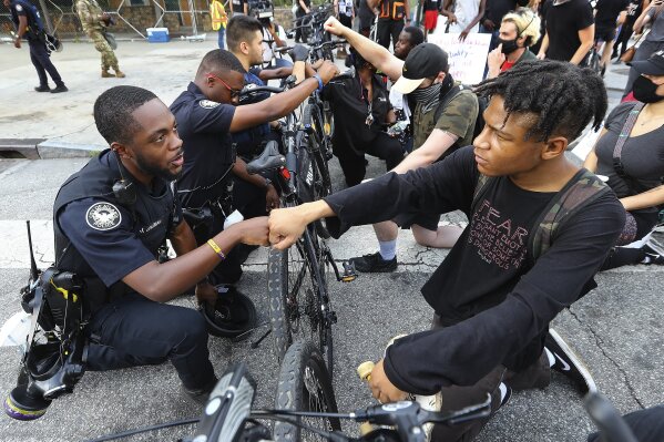 FILE - Atlanta police officer J. Coleman, left, and protester Elijah Raffington fist bump while officers kneel down with protesters in a symbolic gesture of solidarity outside the CNN Center, Wednesday, June 3, 2020, in Atlanta during a protest sparked by the May 25 death of George Floyd in Minneapolis police custody. "These are images from Donald Trump's America today," Democratic presidential nominee Joe Biden said Thursday, Aug. 27, 2020. "The violence we're witnessing is happening under Donald Trump. Not me. It's getting worse, and we know why." (Curtis Compton/Atlanta Journal-Constitution via AP, File)