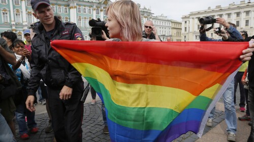 FILE - A police officer speaks with a gay rights activist standing with a rainbow flag, in front of journalists, during a protesting picket at Dvortsovaya (Palace) Square in St. Petersburg, Russia, Aug. 2, 2015. Russian President Vladimir Putin signed new legislation Monday July 24, 2023, that marked the final step in outlawing gender-affirming procedures, a crippling blow to Russia's already embattled LGBTQ+ community. (AP Photo/Dmitry Lovetsky, File)