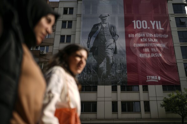 Two women pass by a poster in the backdrop showing an image of Mustafa Kemal Ataturk, to commemorate the 100 year anniversary of modern Turkey, in Istanbul, Turkey, Wednesday, Oct. 25, 2023. The Turkish Republic, founded from the ruins of the Ottoman Empire by the national independence hero Mustafa Kemal Ataturk, turns 100 on Oct. 29. Ataturk established a Western-facing secular republic modeled on the great powers of the time, ushering in radical reforms that abolished the caliphate, replaced the Arabic script with the Roman alphabet, gave women the vote and adopted European laws and codes. (AP Photo/Emrah Gurel)