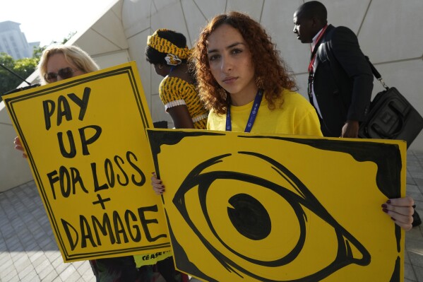 A person holds a sign demanding pay for loss and damage at the COP28 U.N. Climate Summit, Monday, Dec. 4, 2023, in Dubai, United Arab Emirates. (AP Photo/Peter Dejong)