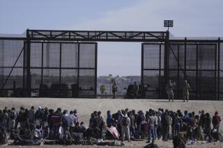 FILE - Migrants who crossed the border from Mexico into the U.S. wait next to the U.S. border wall where U.S. Border Patrol agents stand guard, seen from Ciudad Juarez, Mexico, Thursday, March 30, 2023. The Biden administration will open migration centers in South and Central America for asylum seekers heading to the U.S.-Mexico border, in a bid to slow what’s expected to be a surge of migrants seeking to cross the border next month as pandemic-era immigration restrictions end, U.S. officials said Thursday, April 27. (AP Photo/Fernando Llano, File)