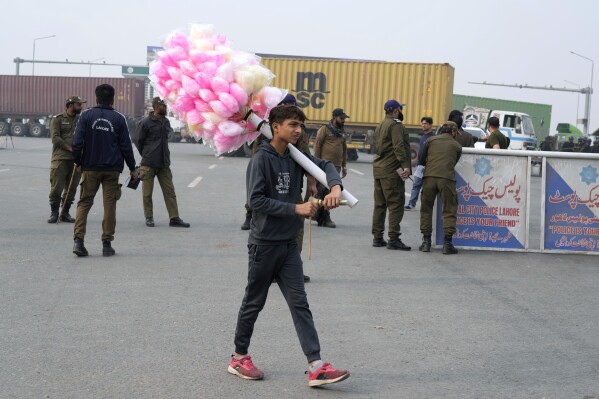 A cotton-candy seller walks past police officers stand guard on an entry point to motorway leading to Islamabad, which has been closed by authorities due to a planned rally by supporters of imprisoned former Prime Minister Imran Khan's Pakistan Tehreek-e-Insaf party, in Lahore, Pakistan, Saturday, Nov. 23, 2024. (AP Photo/K.M. Chaudary)